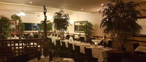 Um restaurante com mesas postas, plantas em vasos e ambiente acolhedor.