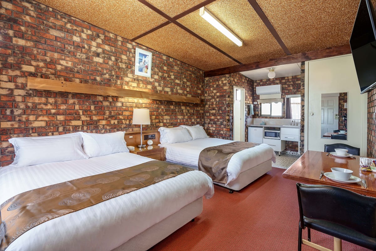 Habitación de hotel con dos camas, una mesa de madera con una silla, un escritorio y un televisor.