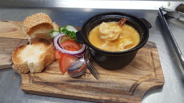 A wooden cutting board with a bowl of soup, slices of bread, and a side salad.