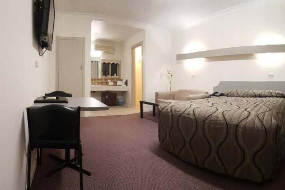 Una habitación de hotel con cama, escritorio, silla, televisión y baño visible a través de una puerta abierta.