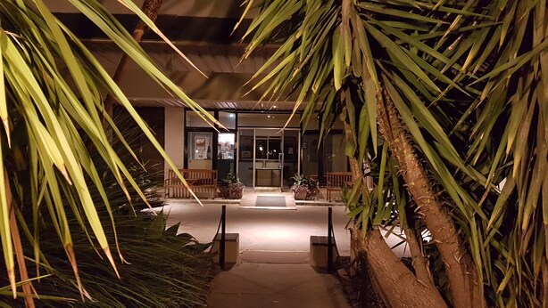 A nighttime view of a building entrance with a pathway leading to a door, surrounded by palm trees and potted plants. - Kerang Valley Resort (Kerang)