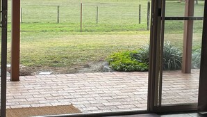 A room with a large sliding glass door leading to a grassy outdoor area with a fence and trees in the background. - Langbrook Estate Cottages (Yarra Junction)