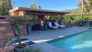 A modern outdoor pool area with a covered patio, lounge chairs, and potted plants. - Langbrook Estate Cottages (Yarra Junction)