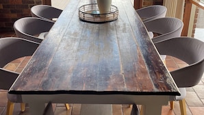 A wooden table with a potted plant in the center, surrounded by chairs, with a view of a green landscape through an open door. - Langbrook Estate Cottages (Yarra Junction)