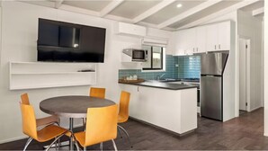 A modern kitchen with white cabinetry, a built-in microwave, a stainless steel refrigerator, and a flat-screen TV mounted on the wall. - Discovery Parks - Mount Buffalo (Porepunkah)