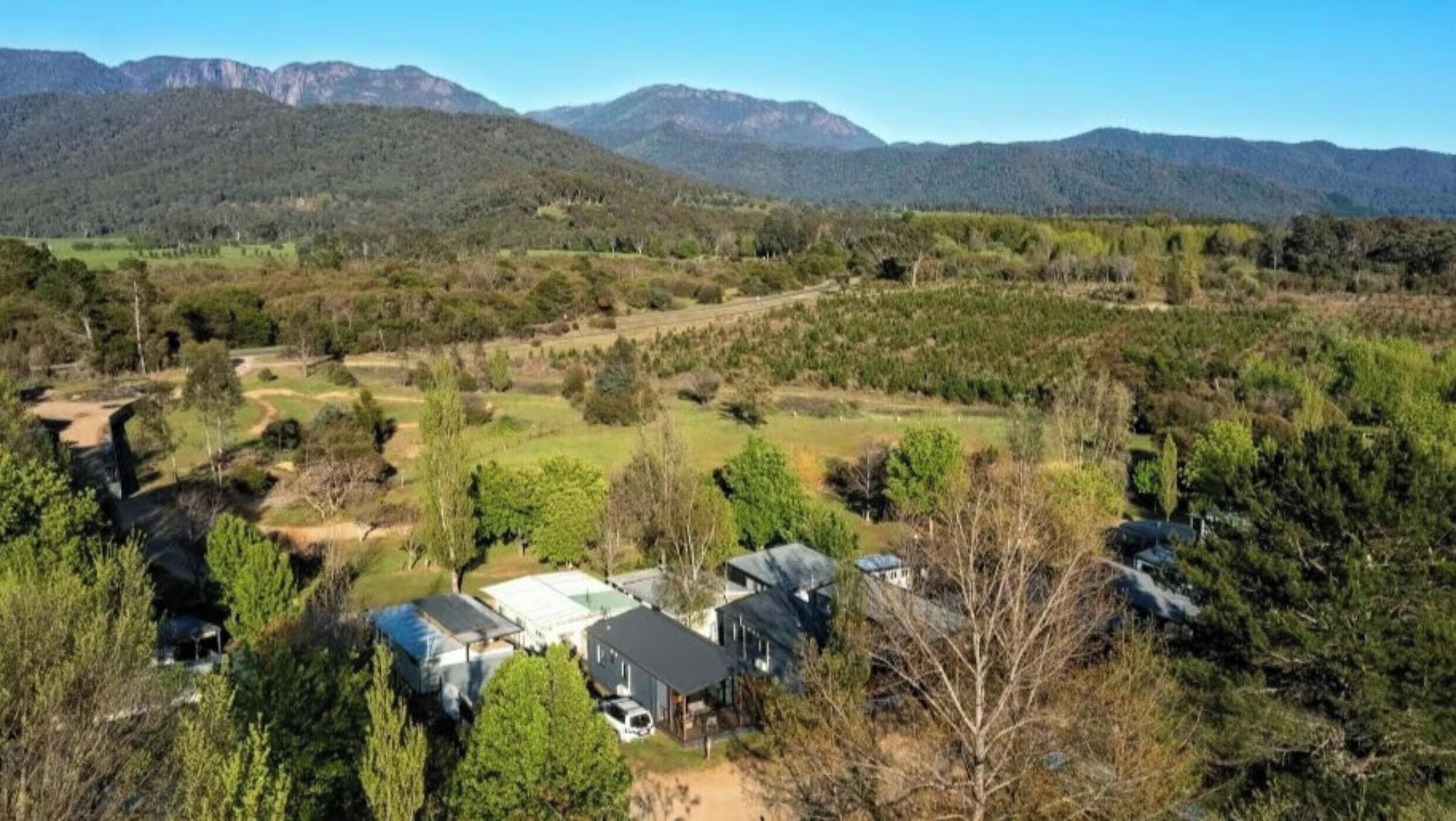 A rural property with multiple buildings, surrounded by dense vegetation and mountains in the background.