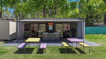 A small outdoor structure with a sign reading "CAMP KITCHEN," featuring a counter and seating area with tables and benches.