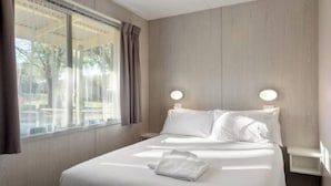 A hotel room with a large bed, two bedside tables, a window with curtains, and a view of the outdoors. - Discovery Parks - Mount Buffalo (Porepunkah)