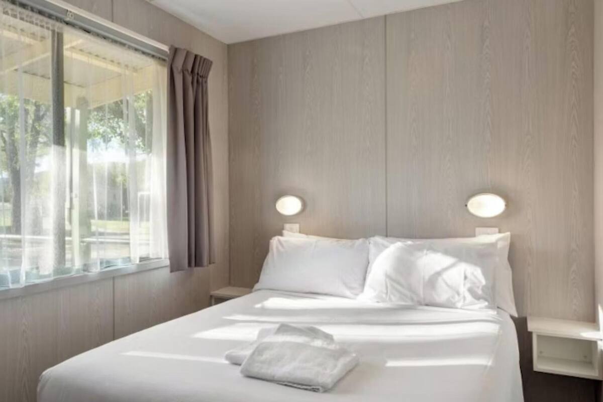 Ein Hotelzimmer mit einem großen Bett, zwei Nachttischen, einem Vorhangfenster und Blick ins Freie.