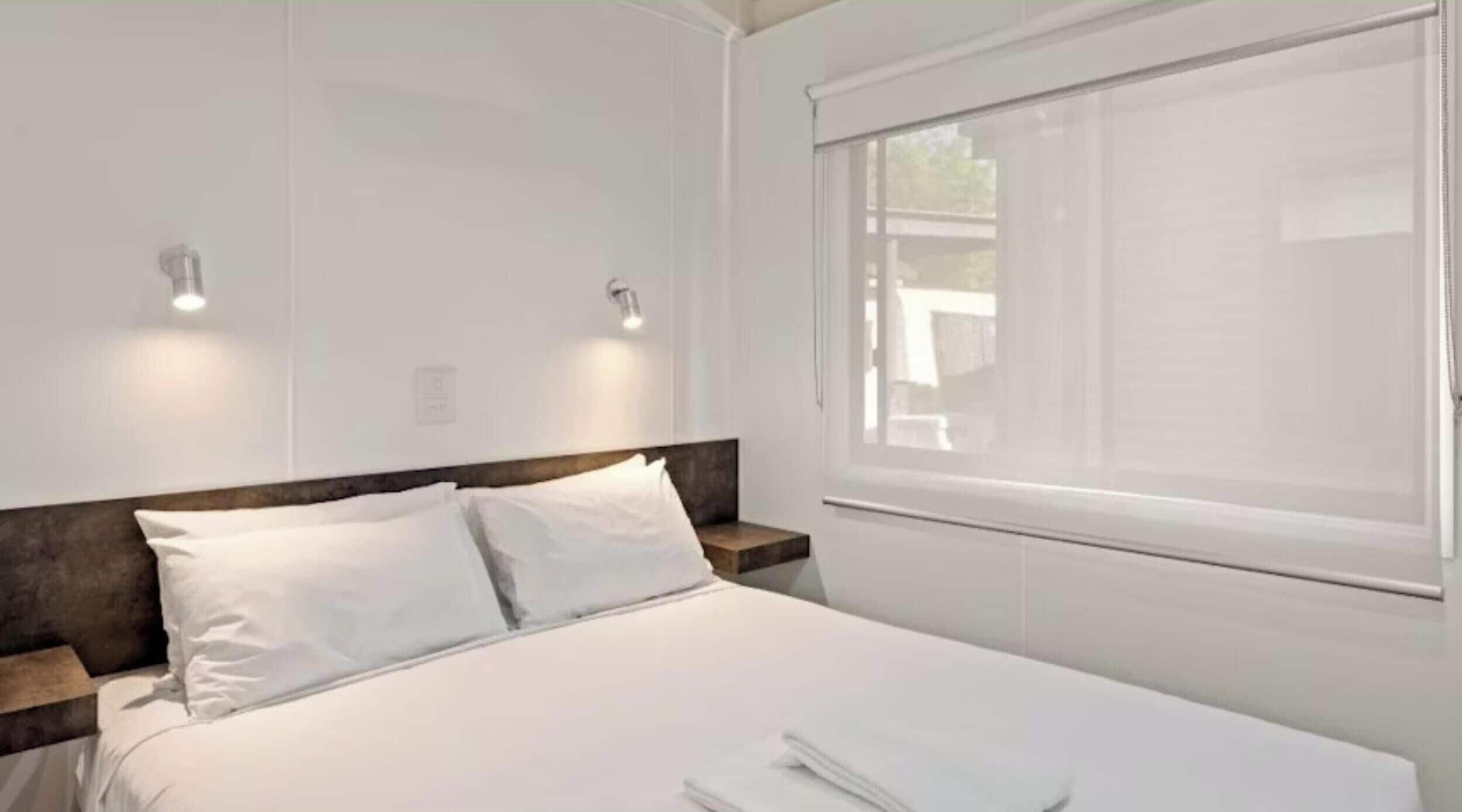 A neatly made bed with white linens, a wooden headboard, and two bedside tables with light fixtures.
