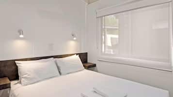 Una cama bien tendida con sábanas blancas, un cabecero de madera y dos mesitas de noche con lámparas.