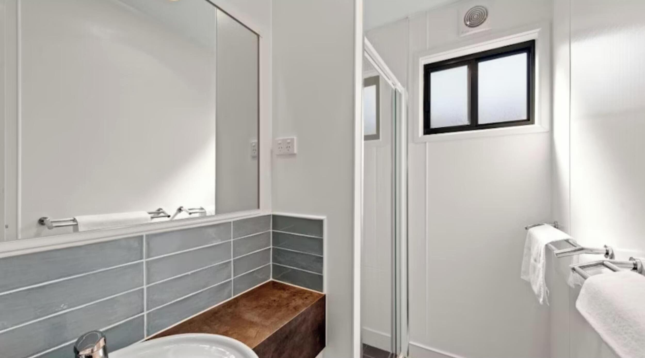 Een badkamer met een grote spiegel, een wastafel, een handdoekhouder en een raam.
