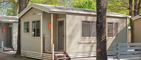 Une petite maison mobile d’un seul étage, dotée d’une véranda et d’une porte, entourée d’arbres.