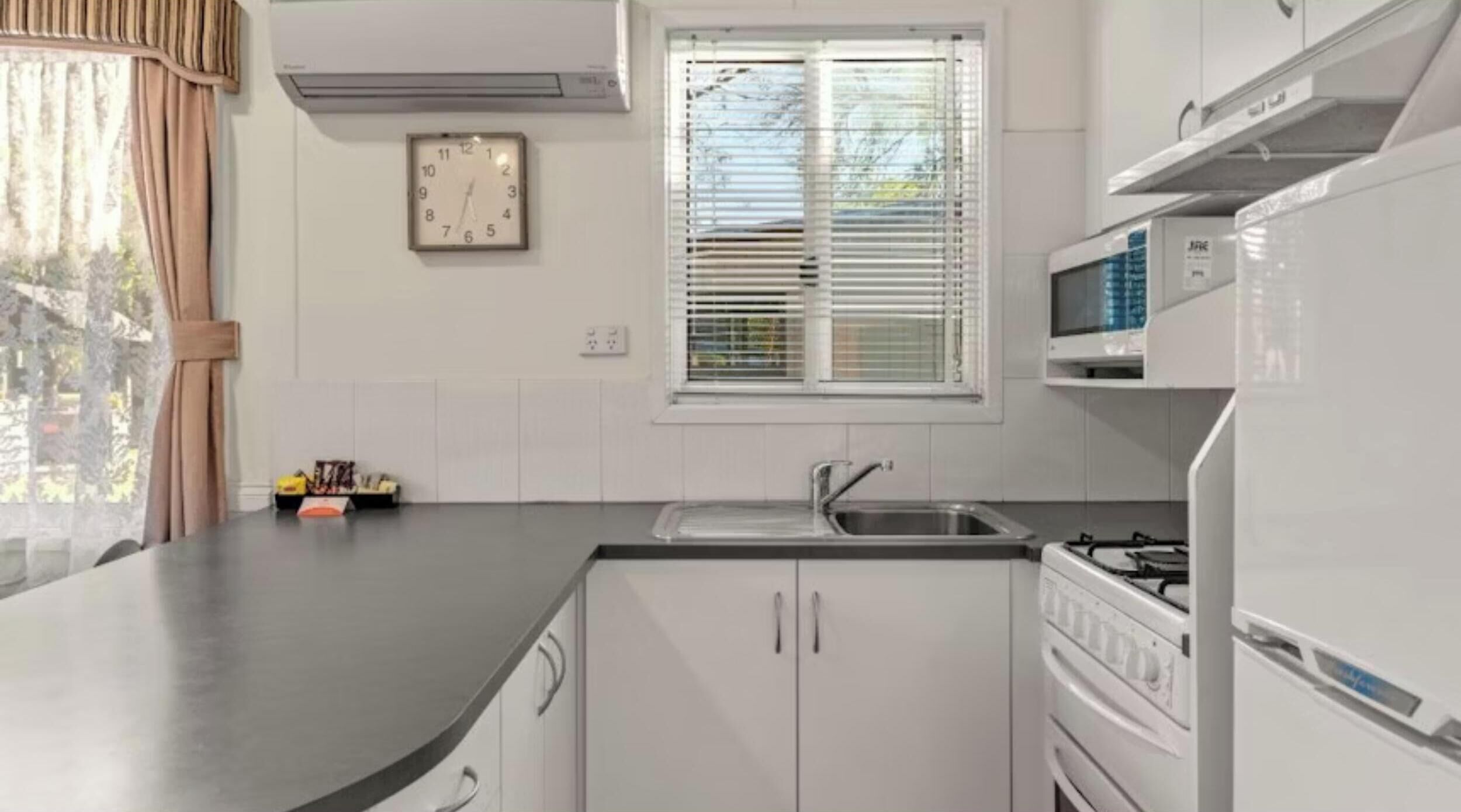 A kitchen with white cabinets, a stainless steel sink, a microwave, and a stove.