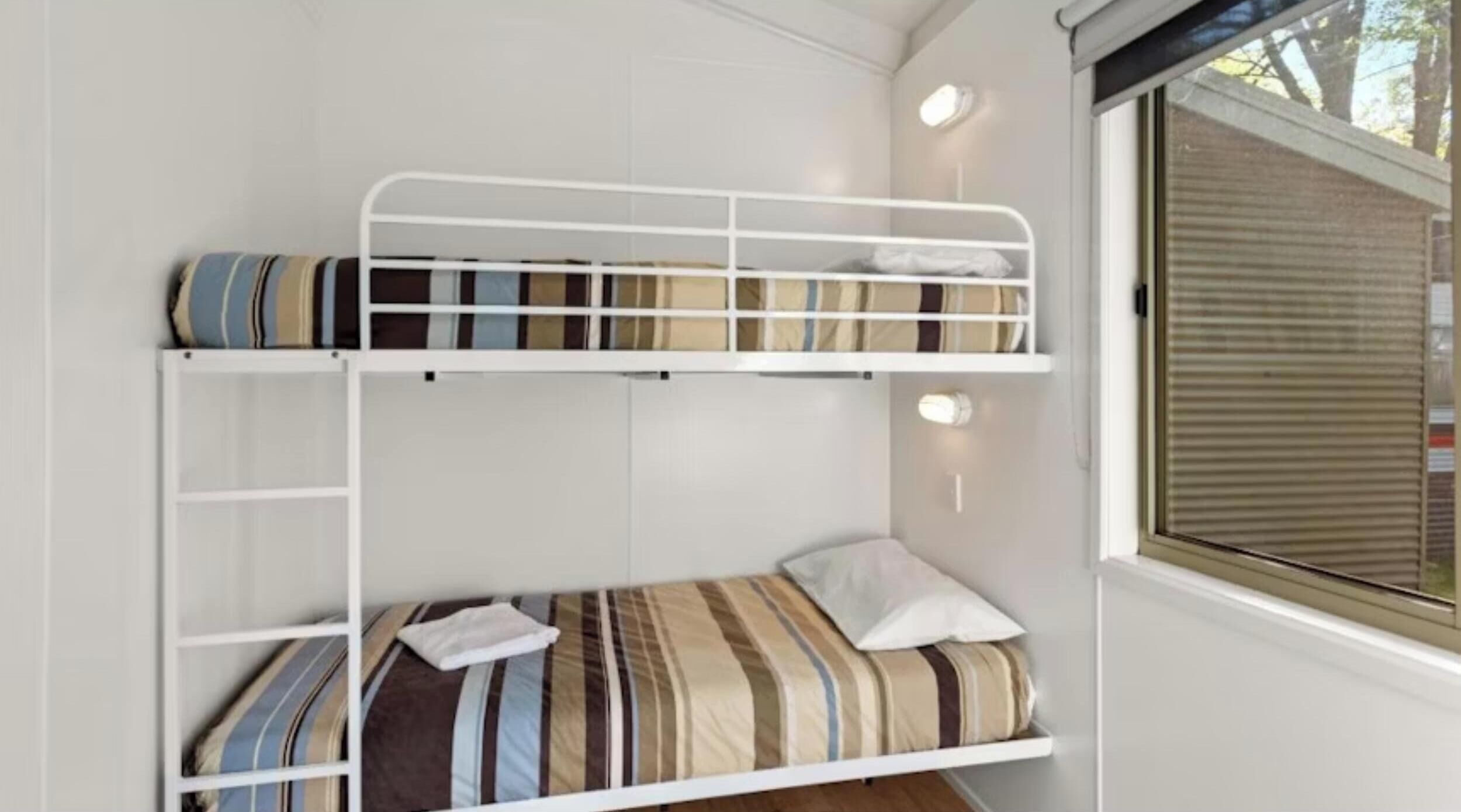 A bunk bed with striped bedding and a window with blinds.