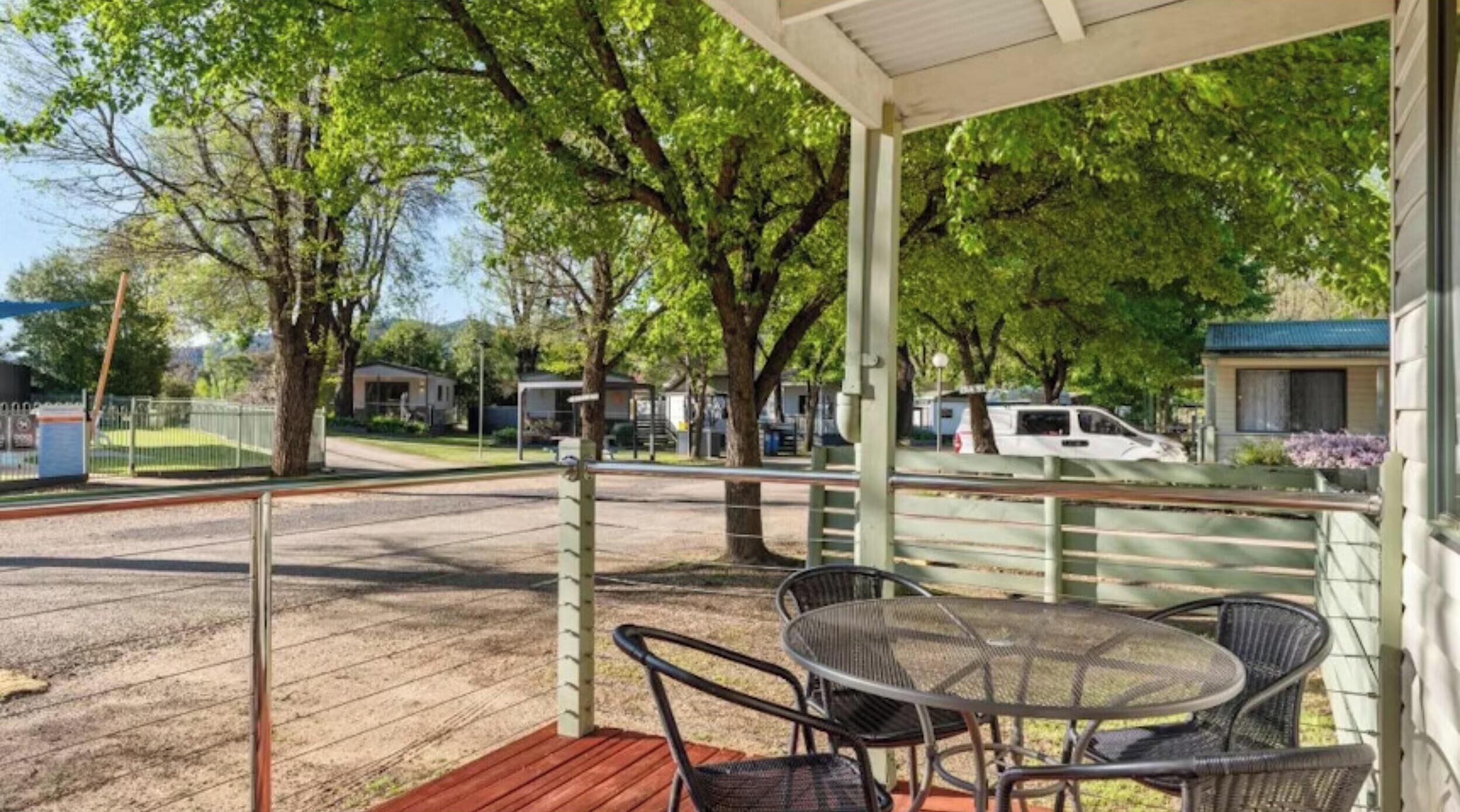 A covered outdoor area with a wooden deck, metal chairs, and a table.