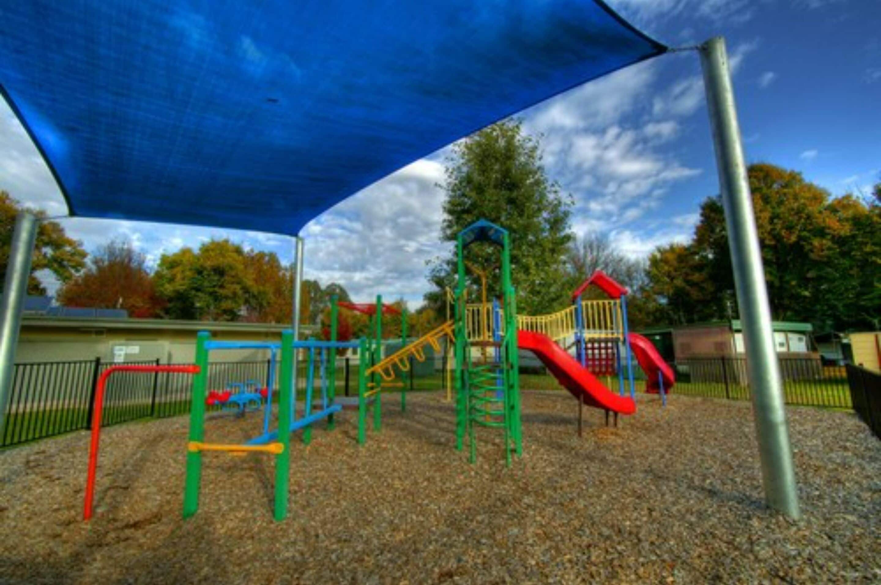 A playground with various play structures, including a slide and climbing frames, covered by a blue canopy.