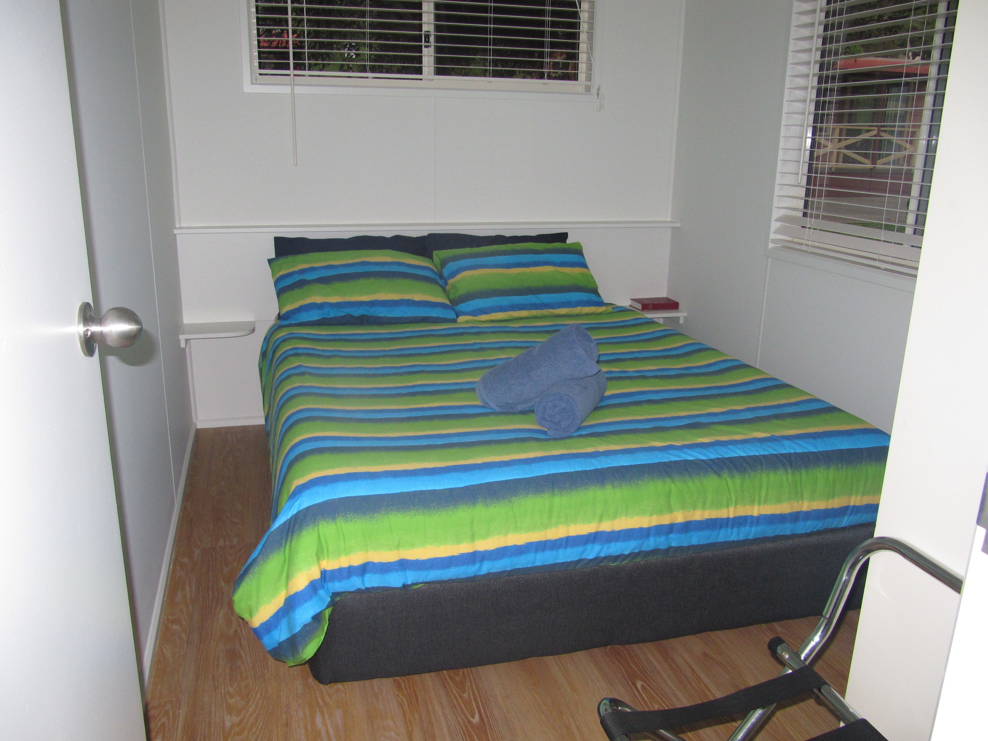 A small, neatly made bed with a colorful striped bedspread and a rolled towel on it.