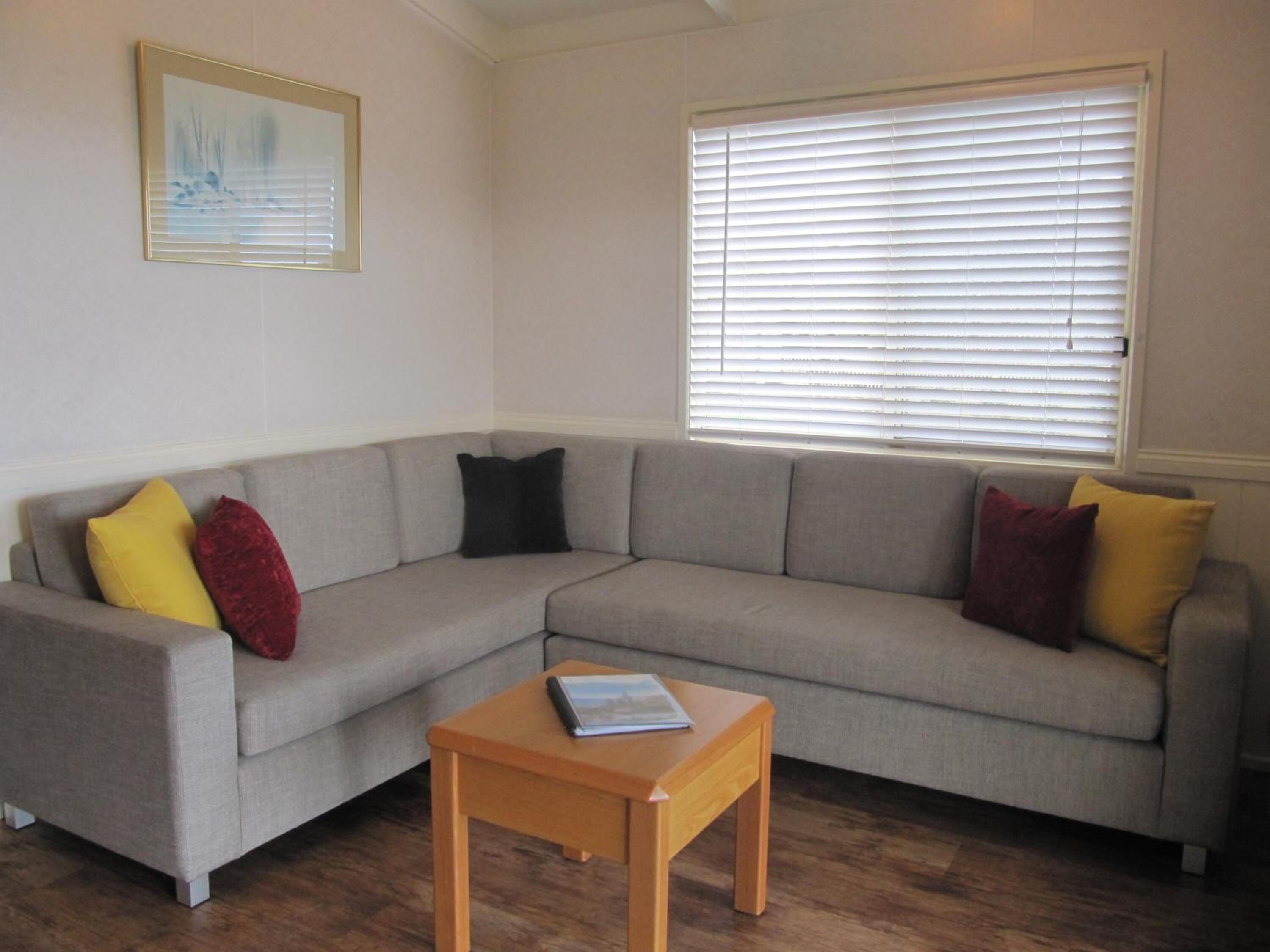 A living room with a grey sectional sofa, a small wooden table, and a window with blinds.