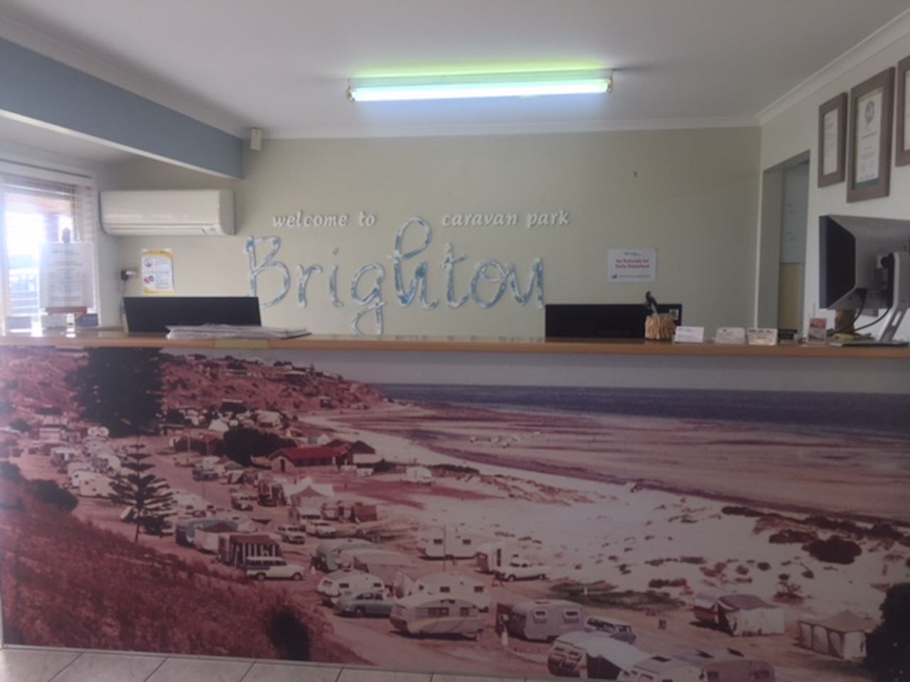 A reception desk with a 'Welcome to Brighton' sign, a flat-screen TV, and a framed certificate on the wall.