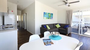 A modern kitchen with a built-in refrigerator and sink, a dining area with a white table and chairs, a gray sofa with colorful cushions, and a balcony with outdoor furniture. - Brighton Beachfront Holiday Park (Kingston Park)