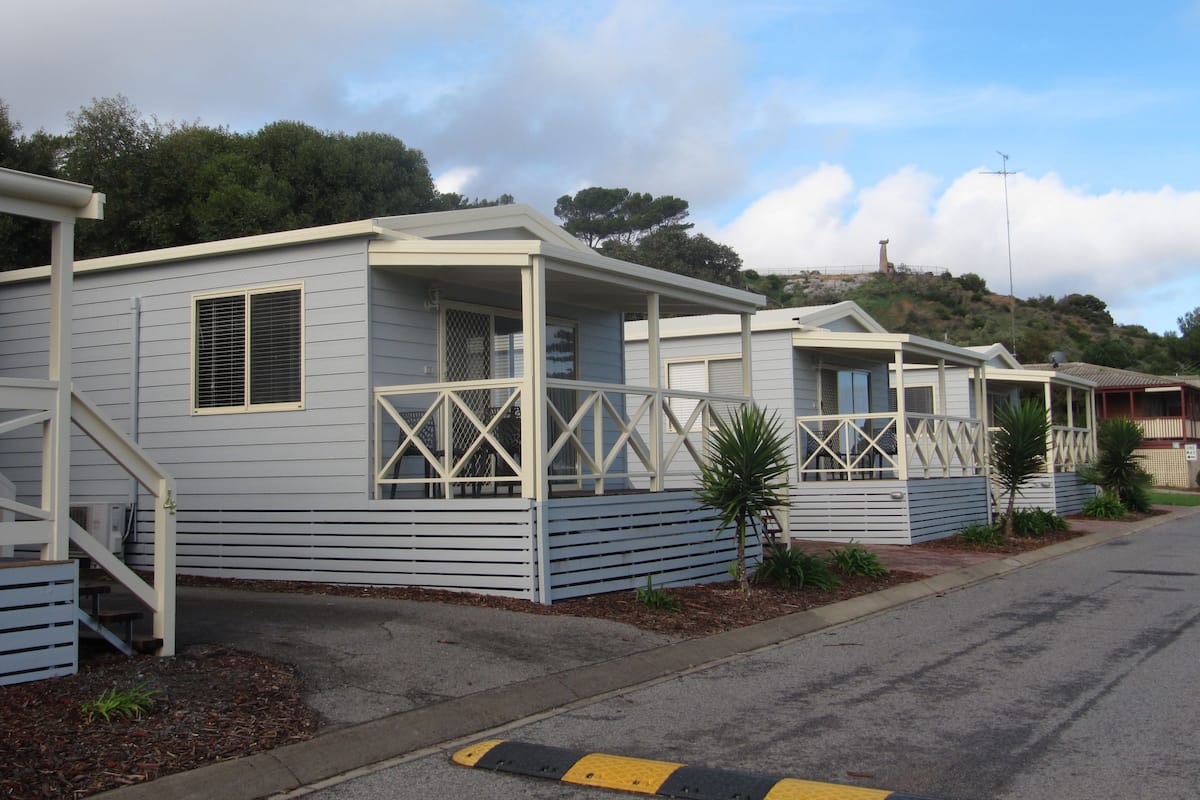 A row of mobile homes with attached porches and a small hill in the background.