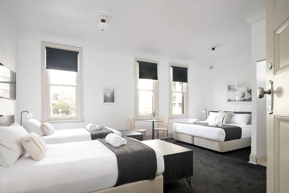 A hotel room with two beds, a small table, and a chair.