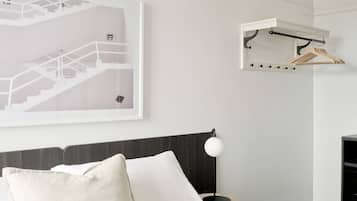 A modern bedroom with a bed, a bedside table, a lamp, a framed abstract artwork, and a wall-mounted drying rack.