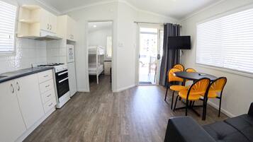 A compact kitchen with white cabinets, a gas stove, and a ceiling fan. There is a dining area with a table and chairs, and a TV mounted on the wall.