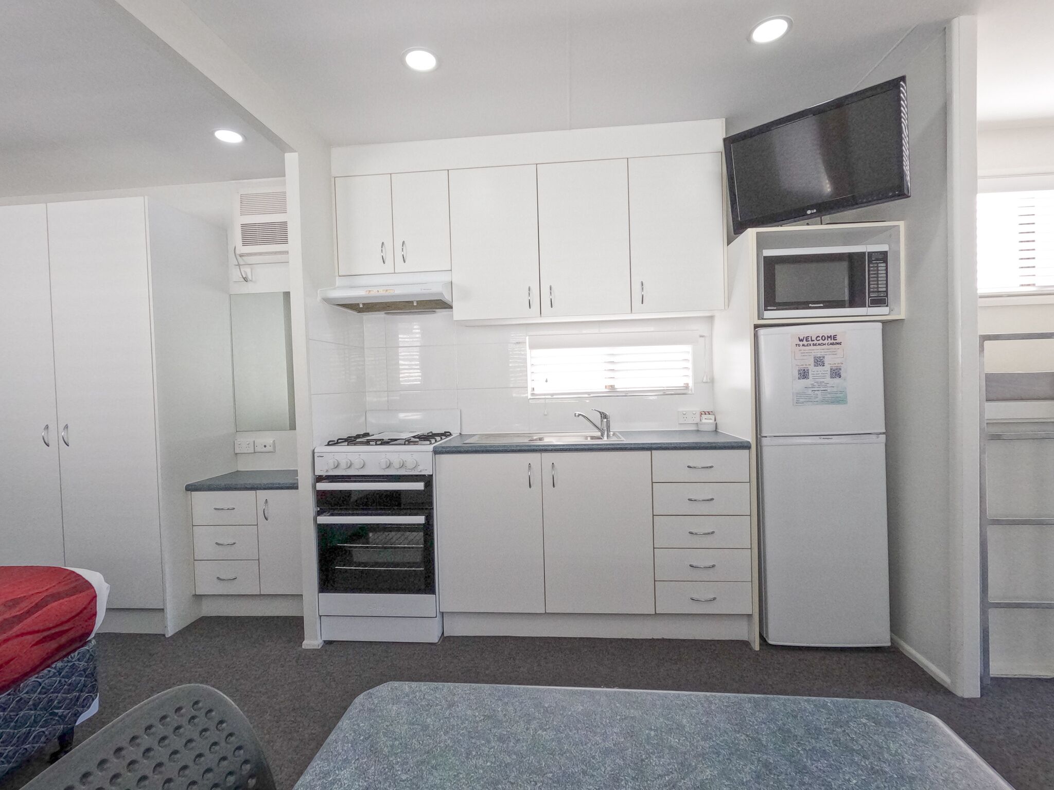 A compact kitchenette with a stove, oven, microwave, and a TV mounted above the microwave.