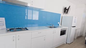 A modern kitchen with white cabinets, a blue backsplash, a gas stove, a sink, and a refrigerator.