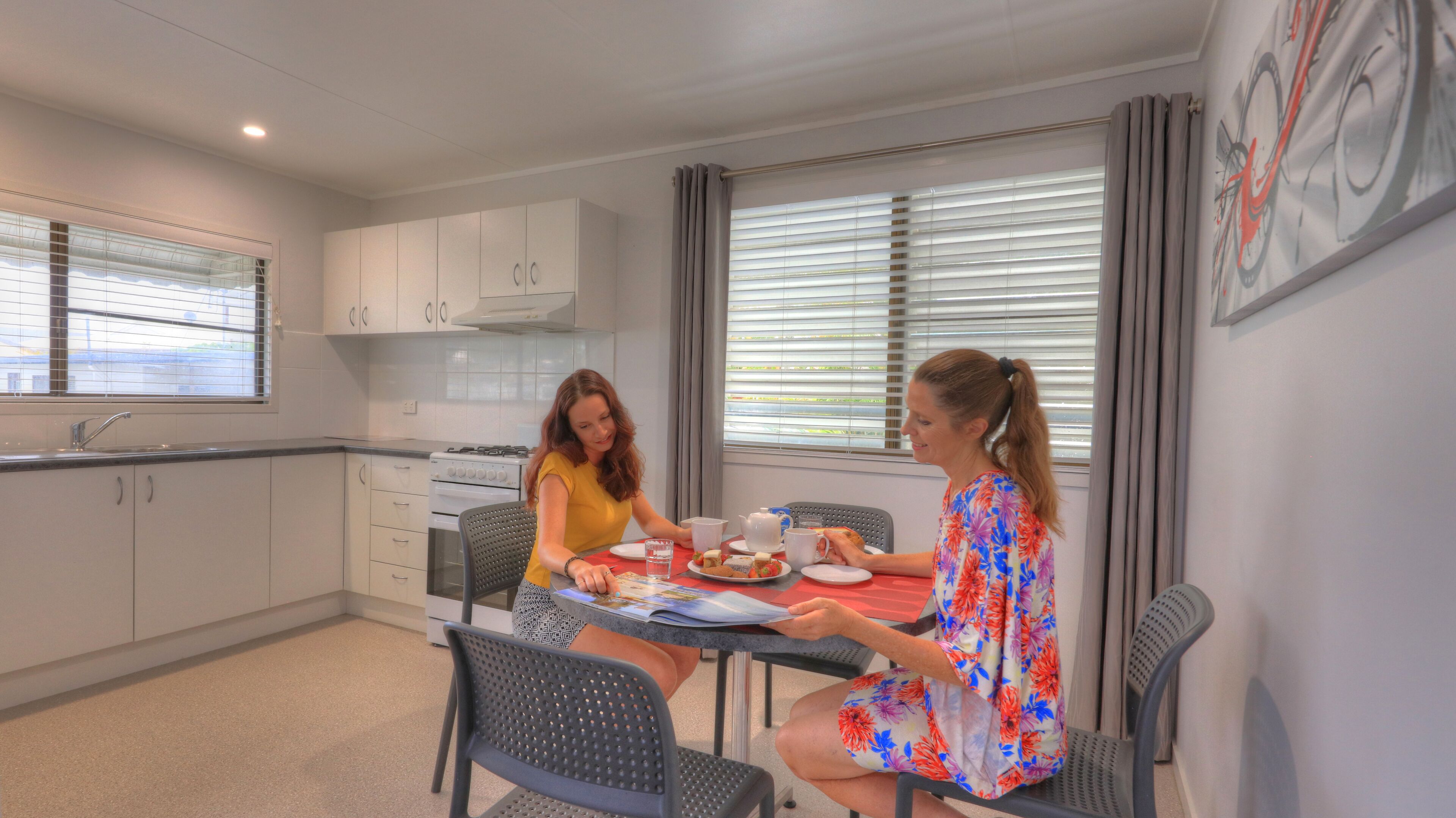 Een moderne keuken met witte kastjes, een gasfornuis en een eethoek met twee stoelen en een tafel.