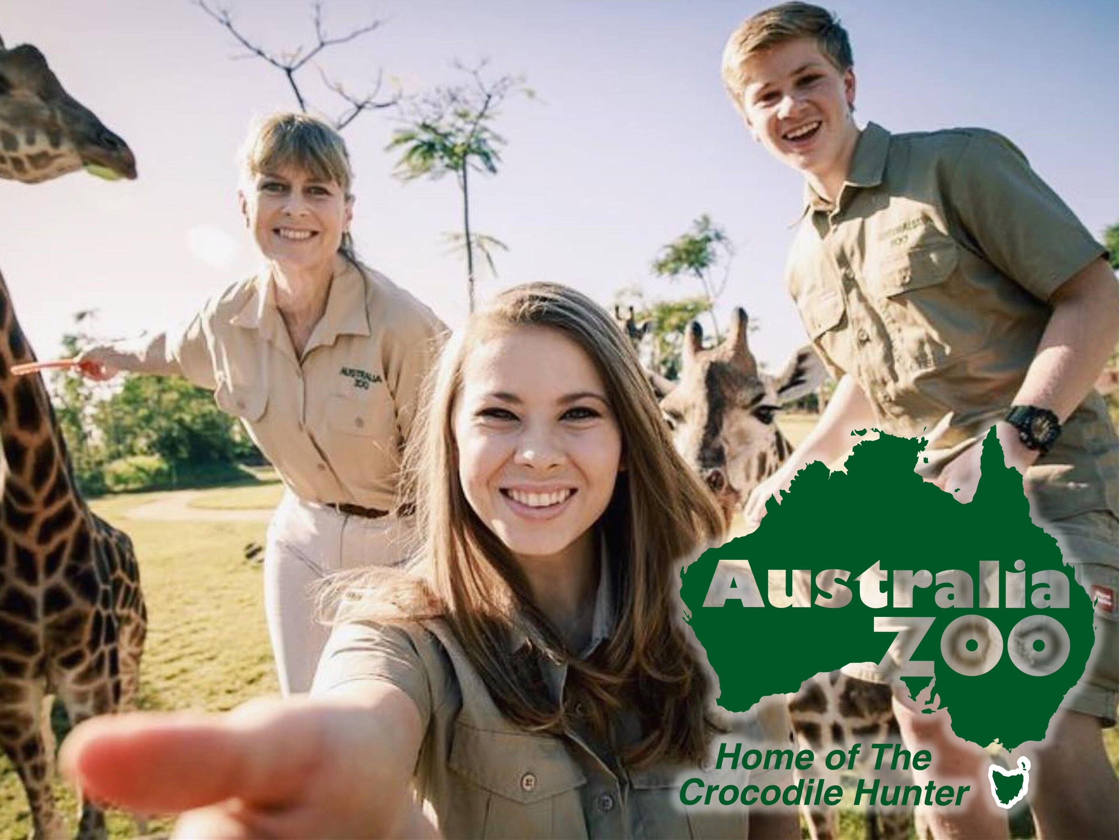 Un groupe de personnes vêtues d’habits de safari au zoo d’Australie, avec des girafes en arrière-plan.