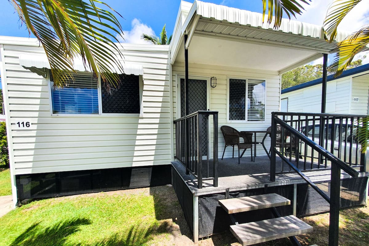 A mobile home with a porch, a small table, and a chair.