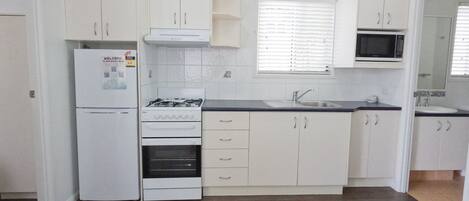 Una cocina con armarios blancos, estufa a gas, microondas y pileta.