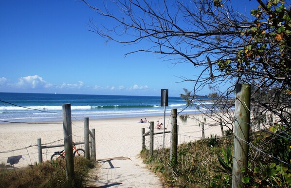 A sandy beach path leading to the ocean with a bicycle and a wooden bench.