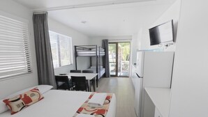Una habitación de hotel con literas, un escritorio, una silla, un televisor y un refrigerador.