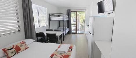 Une chambre d’hôtel équipée d’un lit superposé, d’un bureau, d’une chaise, d’une télévision et d’un réfrigérateur.