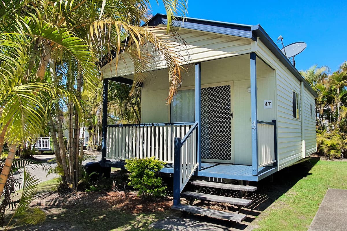 A small, single-story house with a porch, surrounded by palm trees and a well-maintained lawn.