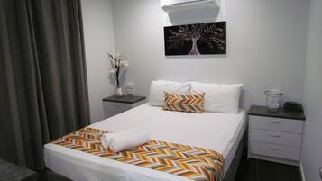 Una camera d'albergo con un letto, un comodino, un tavolino, un condizionatore d'aria e un quadro appeso al muro.