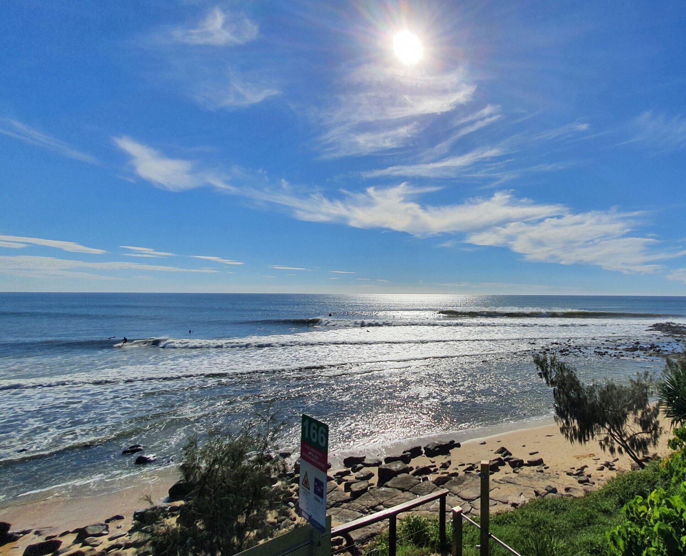 A beach with a rocky shoreline, a sign with the number 166, and a clear blue sky.