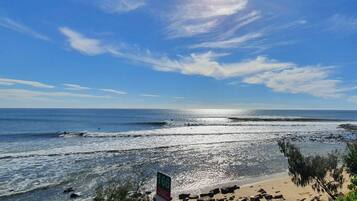 A beach with a rocky shoreline, a sign with the number 166, and a clear blue sky.
