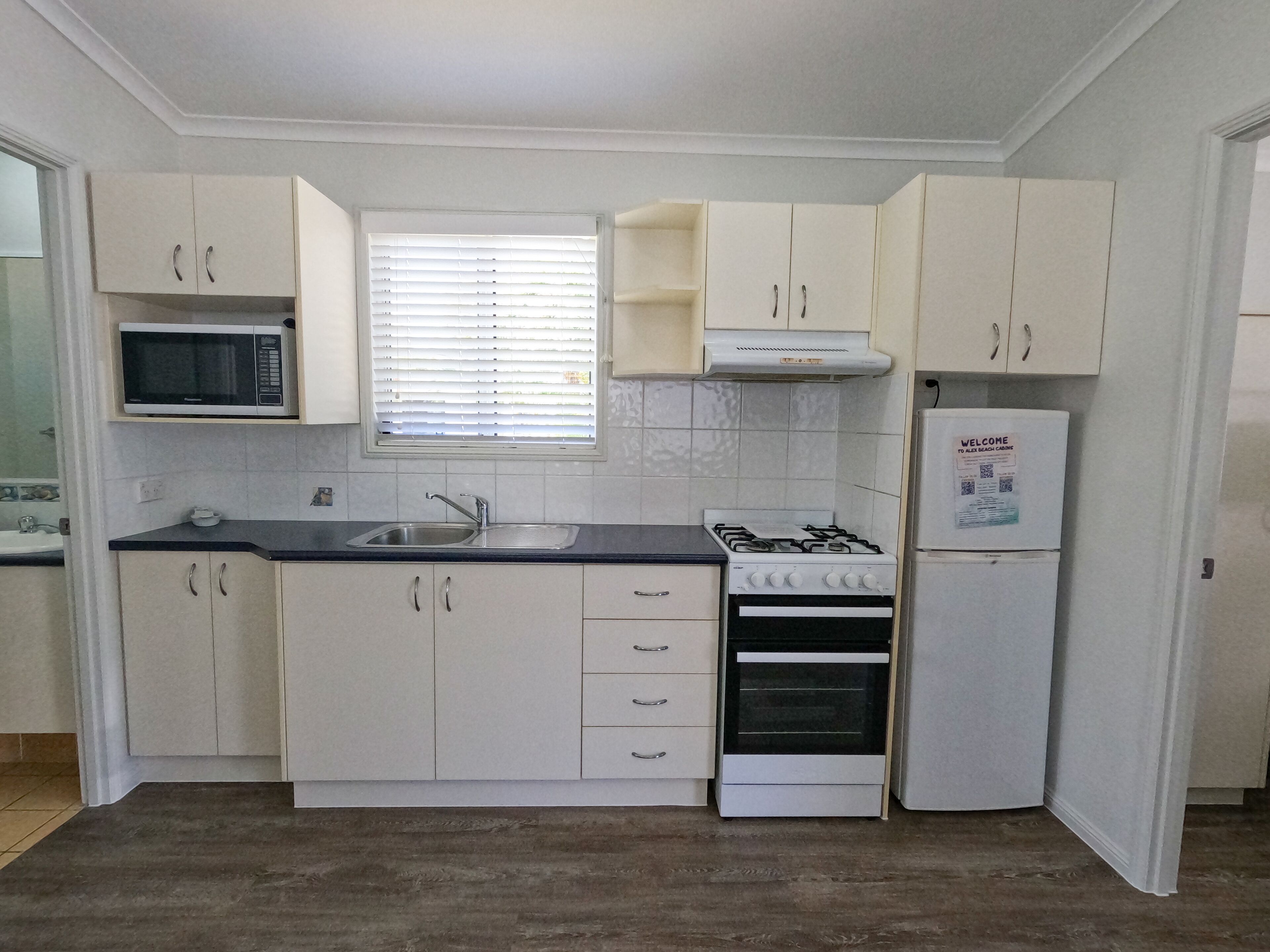 Una cocina con armarios blancos, microondas, estufa y refrigerador.