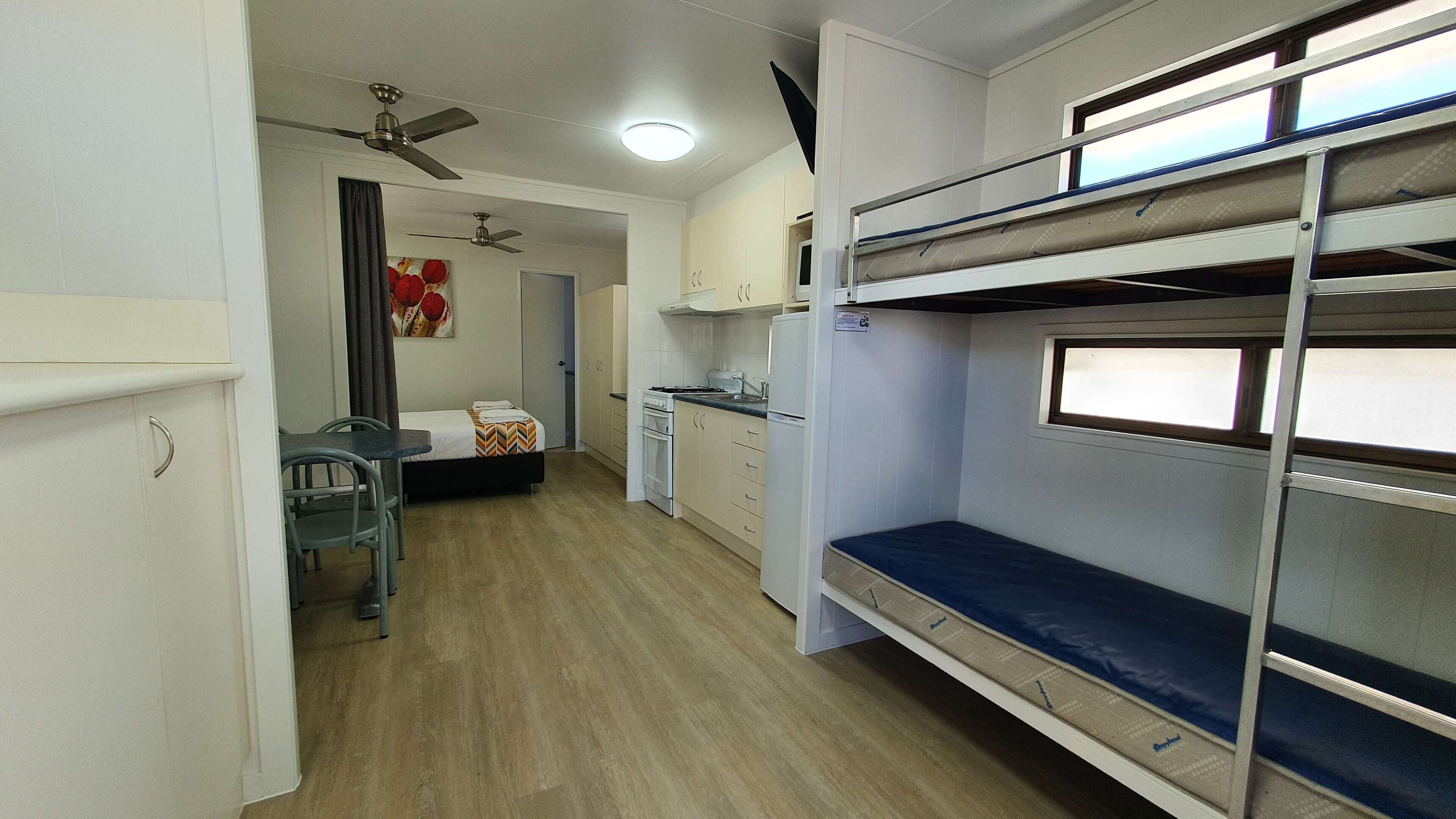 Habitación de hotel compacta con literas, kitchenette, pequeño comedor y ventilador de techo.