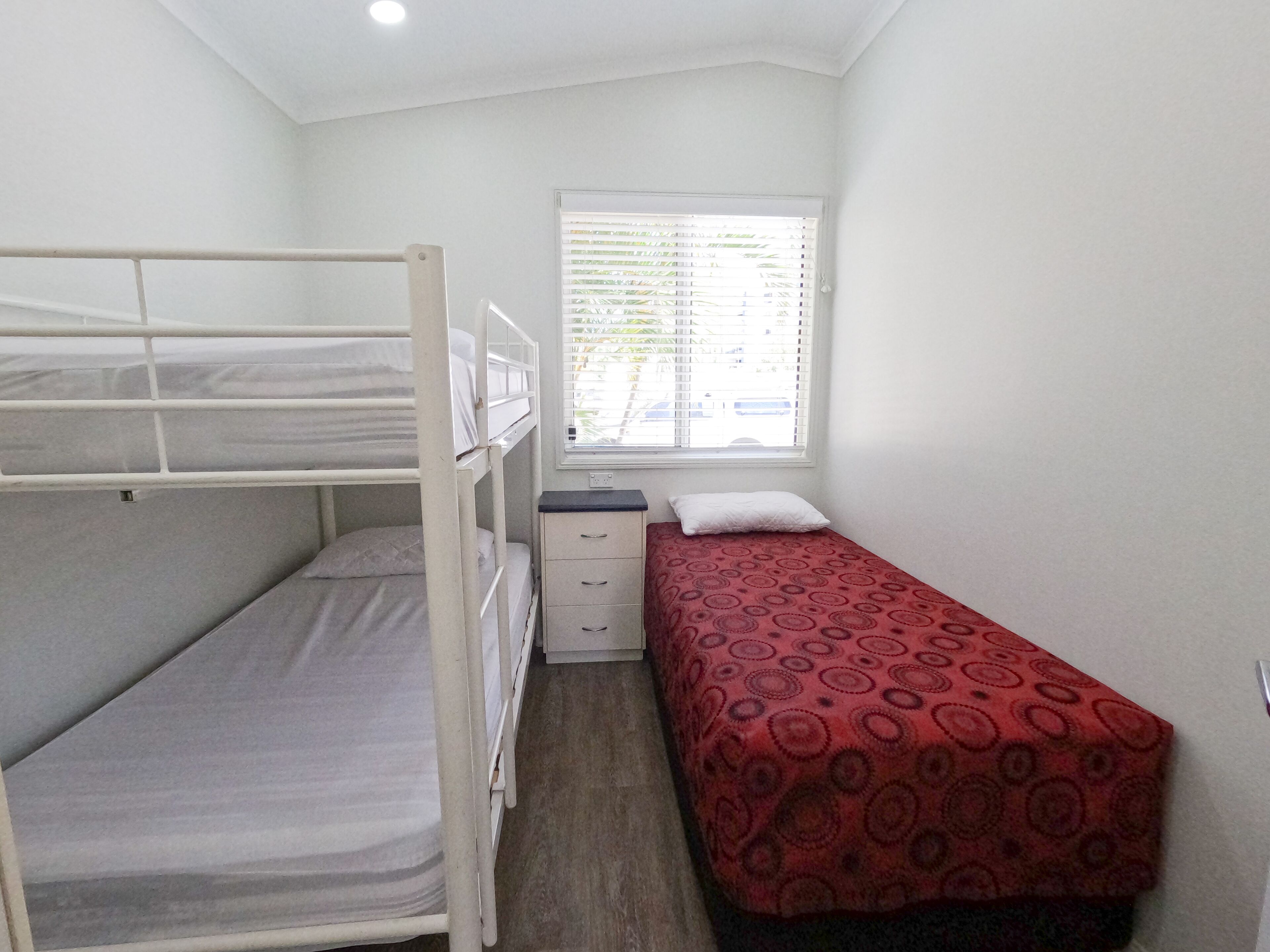 Habitación tipo dormitorio con literas, una cama individual, un escritorio pequeño y una ventana con persianas.