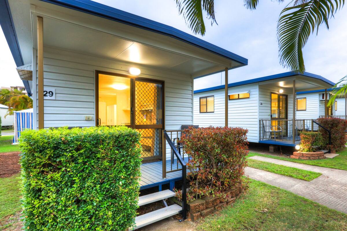A row of blue mobile homes with numbered doors, a covered porch, and a well-maintained lawn.