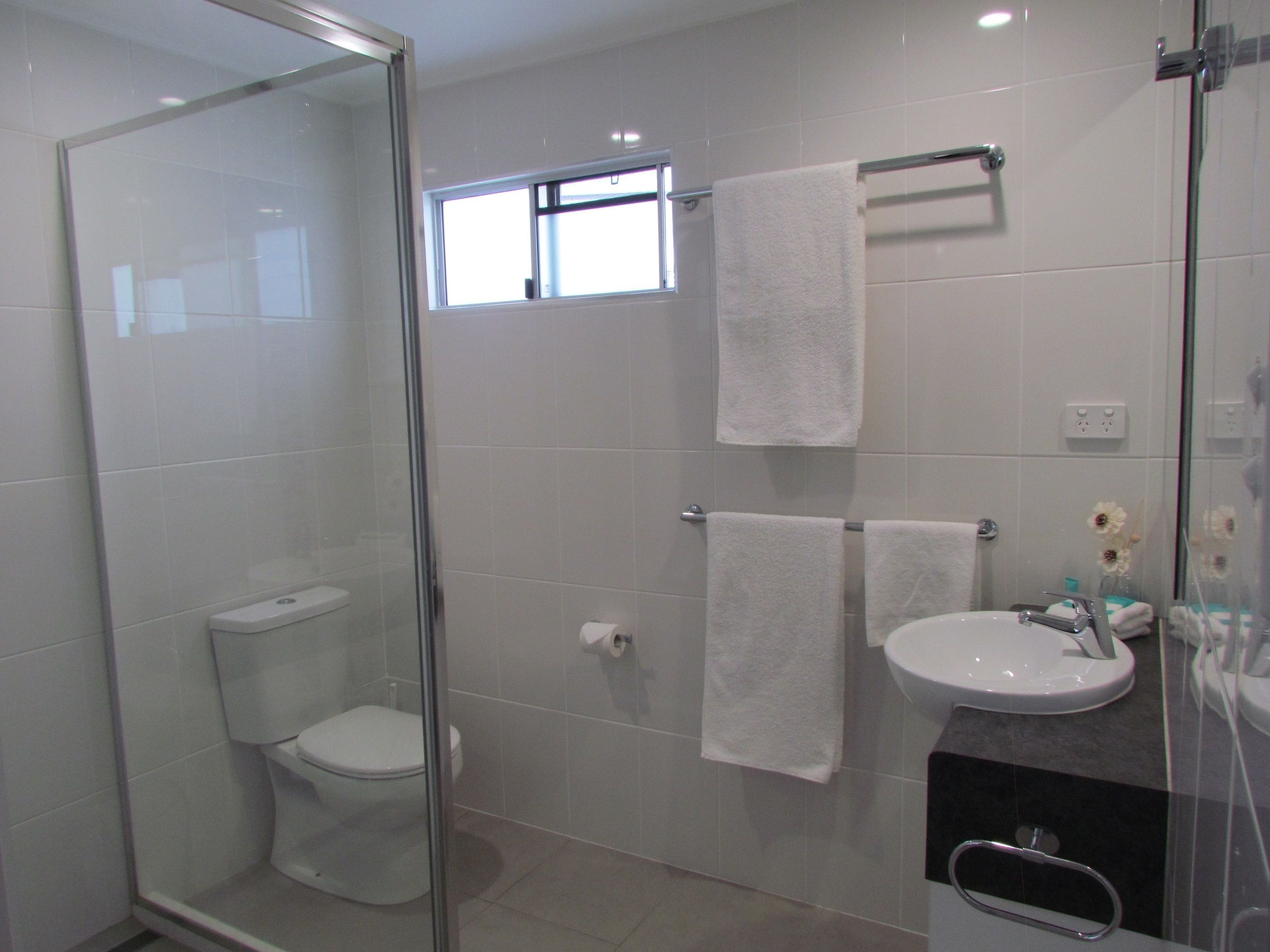Un baño moderno con cabina de ducha de vidrio, inodoro, lavabo y dos toallas colgadas en un perchero.
