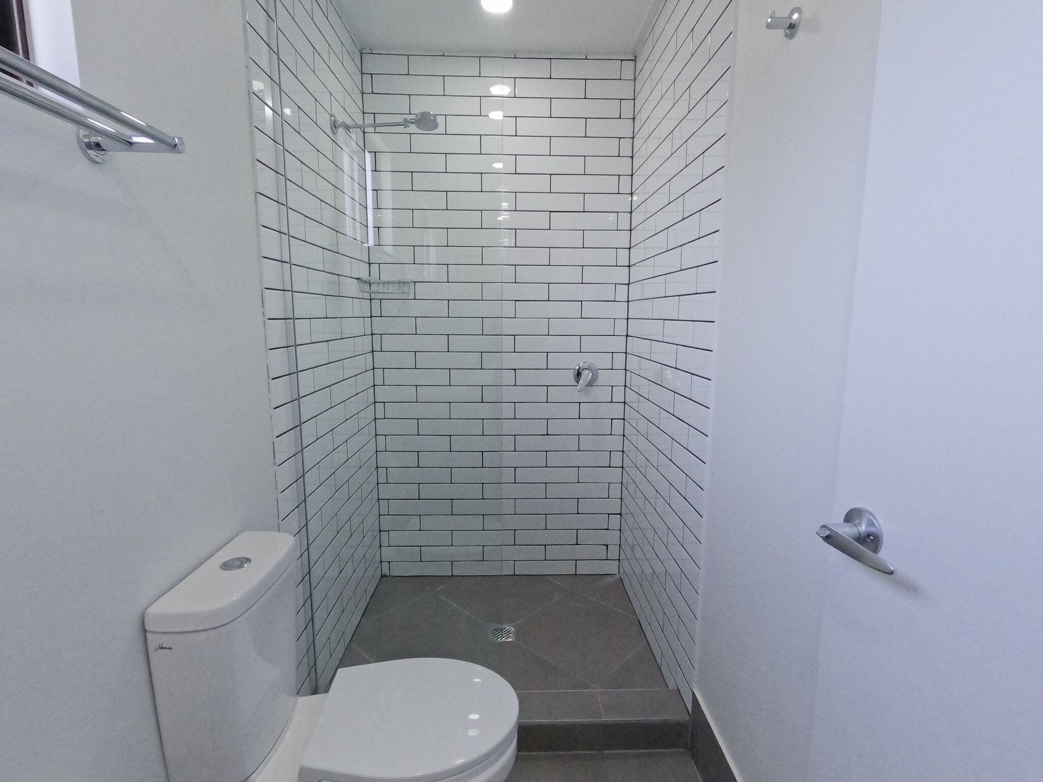Une petite salle de bain étroite aux murs recouverts de carreaux blancs et aux toilettes blanches.