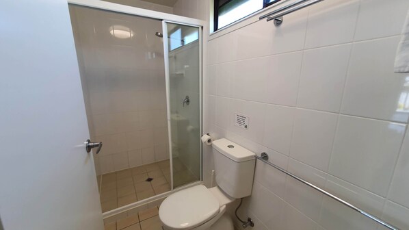 A bathroom with a toilet, a glass shower enclosure, and a white tiled wall.