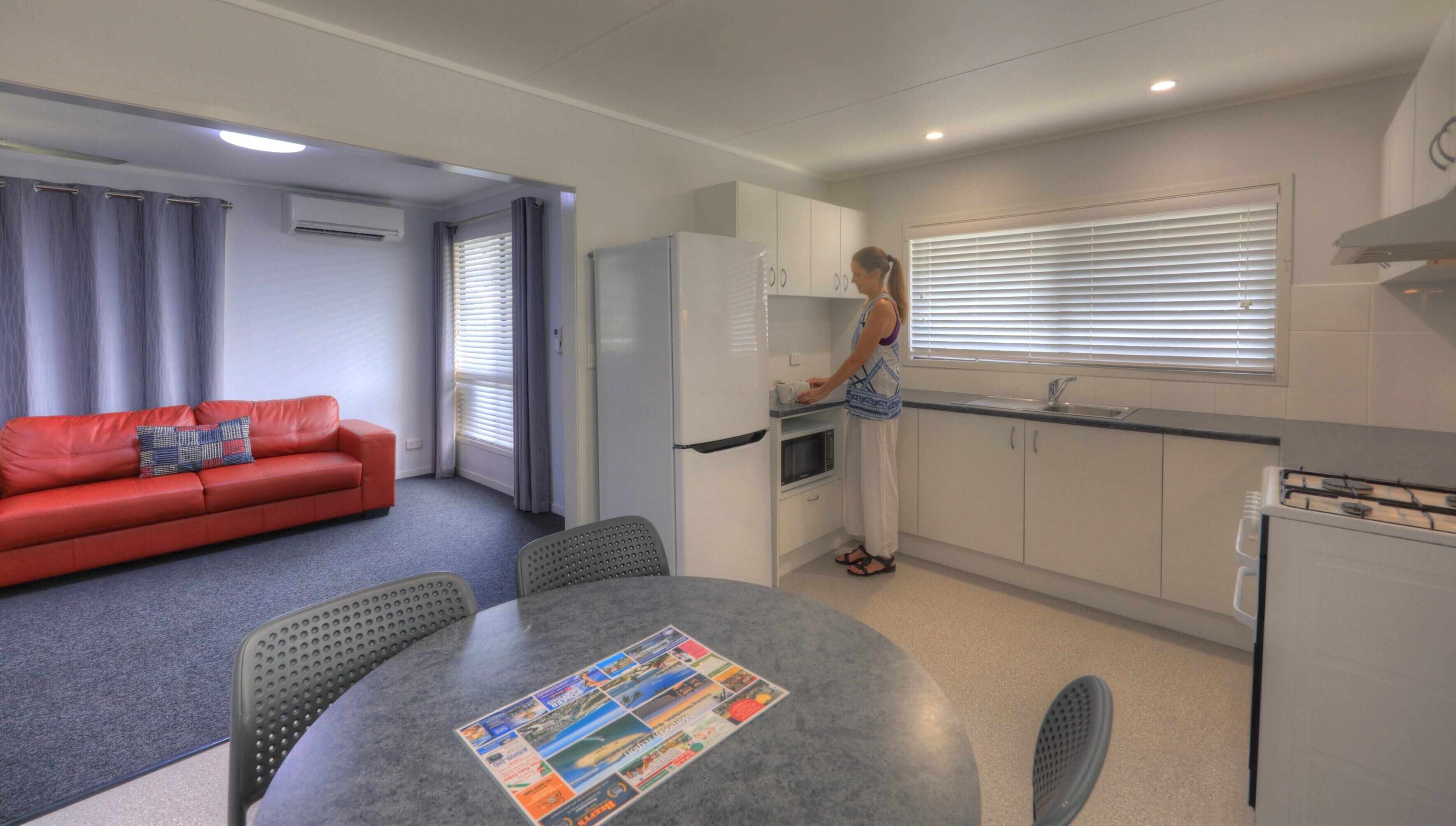 Un espacio habitable compacto con kitchenette, zona de comedor y sofá rojo.